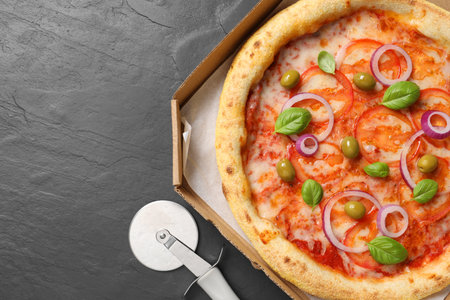 Delicious vegetarian pizza in box and cutter on black table, top view. Space for textの写真素材