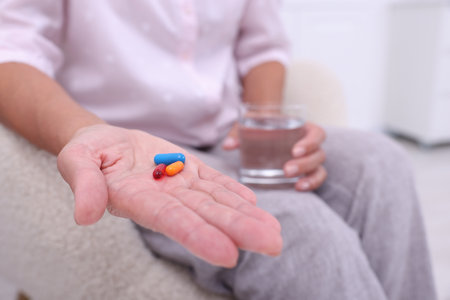 Senior woman with pills and glass of water at home, closeupの写真素材