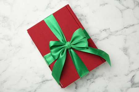 Book tied with green ribbon on white marble table, top view