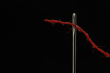 Sewing needle with red thread on black background, closeup. Space for text