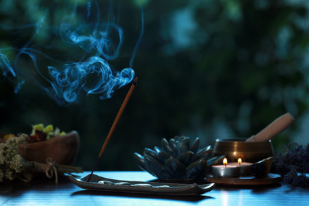 Incense stick smoldering in holder, burning candles, dry flowers and Tibetan singing bowl on wooden table outdoorsの写真素材