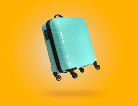 Turquoise suitcase in air on orange backgroundの写真素材