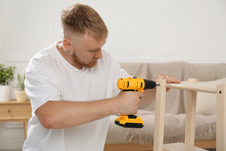 Man with electric screwdriver assembling furniture in roomの写真素材