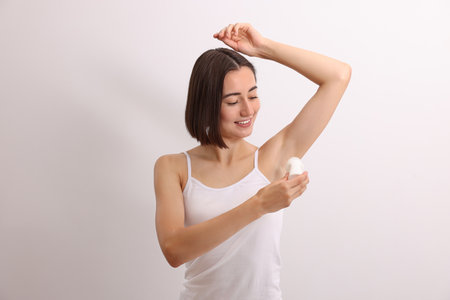 Smiling woman applying roll-on deodorant on white backgroundの写真素材