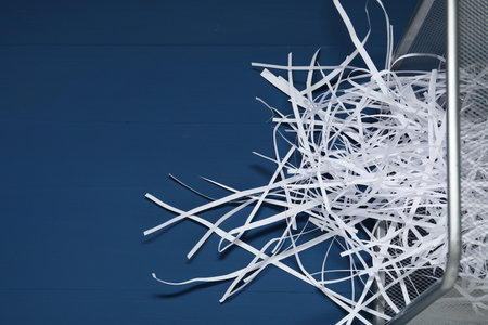 Shredded paper strips in trash bin on blue wooden table. Space for textの写真素材