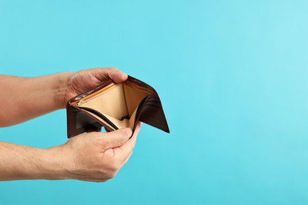 Man with empty wallet on light blue background, closeup. Space for text