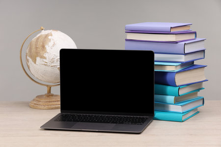 Stack of colorful books, globe and laptop on white wooden table against light grey backgroundの写真素材