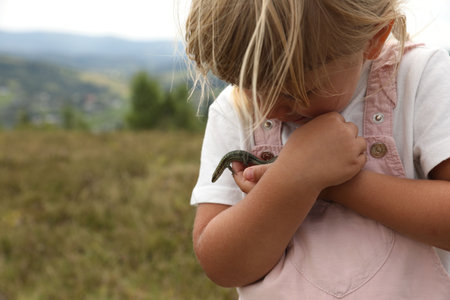 Cute little girl holding lizard at field, space for text. Child enjoying beautiful natureの写真素材