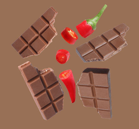 Pieces of chocolate and chili pepper in air on brown background