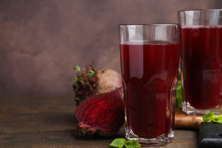 Fresh beet juice in glasses and ripe vegetables on wooden table, closeup. Space for textの写真素材