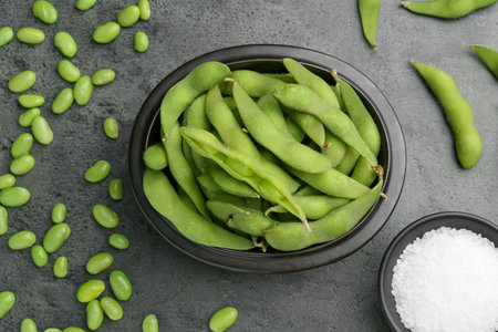 Raw green edamame soybeans and pods on gray table, flat lay