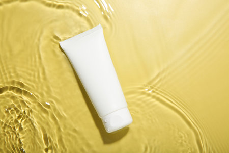 Tube with cream in water on yellow background, top view. Cosmetic product