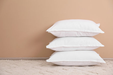 Stack of white pillows on floor near beige wall. Space for textの写真素材