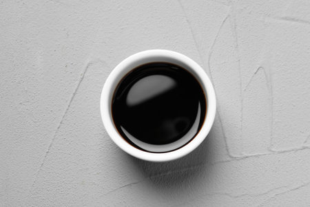 Balsamic vinegar in bowl on light gray textured table, top view