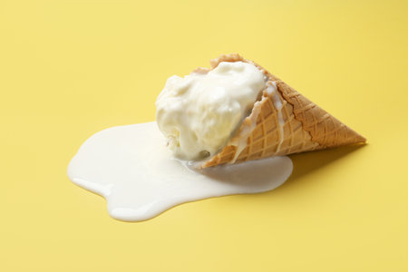 Melted ice cream in wafer cone on yellow backgroundの写真素材
