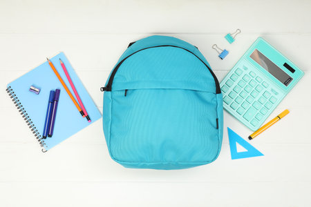 Backpack and different school supplies on white wooden background, flat lay