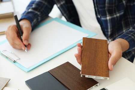 Man taking notes at table with different samples of wooden flooring indoors, closeupの写真素材