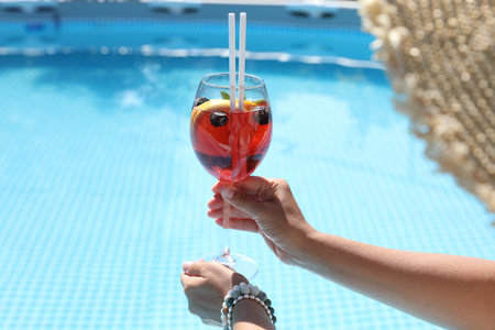 Woman holding tasty cocktail in glass near swimming pool outdoors, closeup