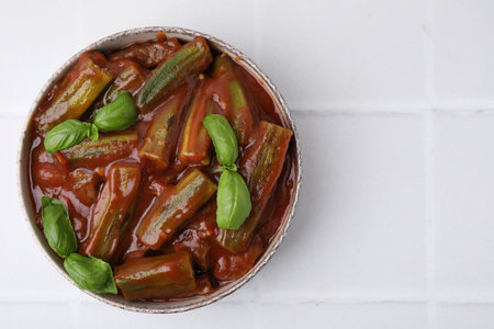 Tasty stew with okra, tomato sauce and basil on white tiled table, top view. Space for textの写真素材