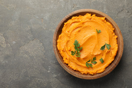 Delicious mashed sweet potatoes with parsley in bowl on gray textured table, top view. Space for textの写真素材