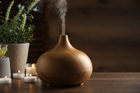 Aroma oil diffuser, burning candles and houseplants on wooden table, space for textの写真素材