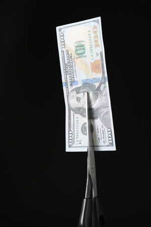 Budgeting. Cutting dollar banknote with scissors on black background, closeupの写真素材