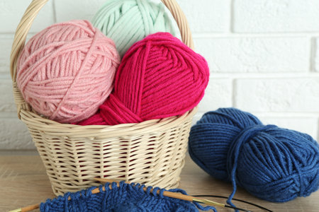 Bright yarns, knitting needles and pattern sample on wooden shelf indoors, closeup