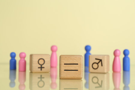Gender equality concept. Wooden cubes with male and female figures on light yellow background,...