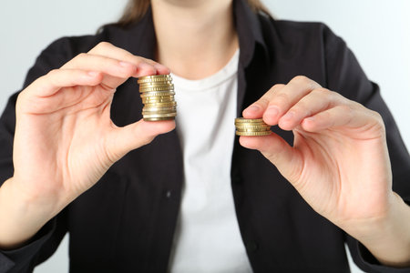 Financial inequality. Woman comparing two stacks of coins on white background, closeupの写真素材