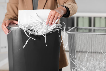 Woman destroying sheets of paper with shredder in office, closeupの写真素材