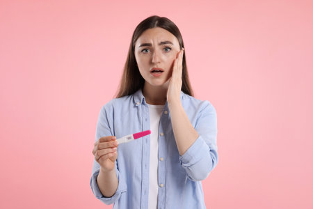 Shocked woman holding pregnancy test on pink backgroundの写真素材