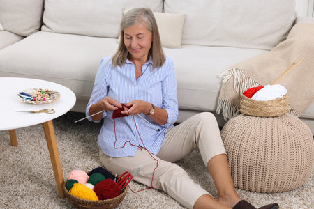 Smiling senior woman knitting near sofa at homeの写真素材