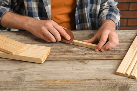 Man polishing wooden plank with sandpaper at table, closeup