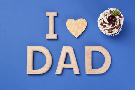 Happy Father's Day. Phrase I love Dad made with wooden letters, decorative heart and cupcake on blue background, flat layの写真素材