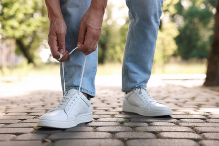 Man tying shoelace of white sneaker outdoors, closeupの写真素材