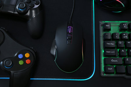Computer mouse, RGB keyboard and game controllers on black background, top view