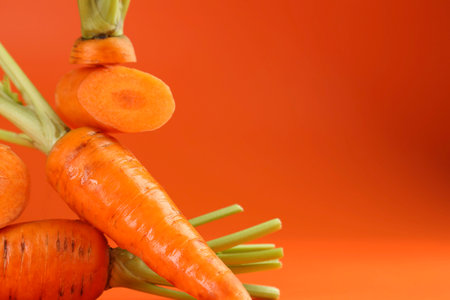 Whole and cut fresh carrots on orange background, closeup. Space for textの写真素材