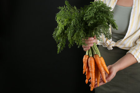 Woman holding ripe carrots on black background, closeup. Space for textの写真素材