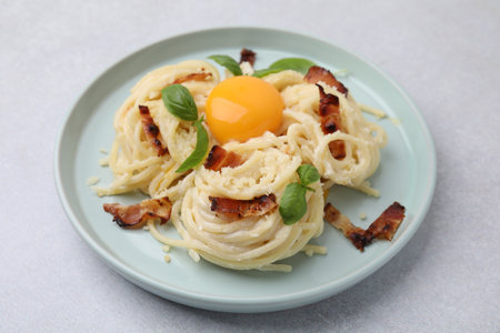 Delicious pasta Carbonara with egg yolk, bacon and basil on light gray table, closeupの写真素材