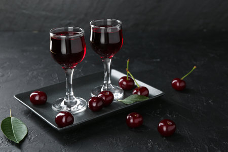 Delicious cherry liqueur in glasses and berries on black table. Space for textの写真素材