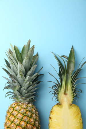 Whole and cut ripe pineapples on light blue background, flat lay. Space for text