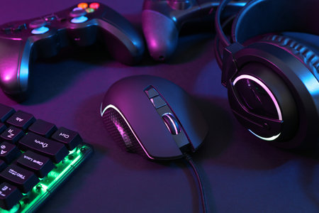 Computer mouse, headset, RGB keyboard and game controllers in neon lights on dark background,...