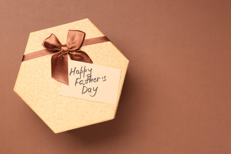 Card with phrase Happy Father's Day and gift box on light brown background, top view. Space for text