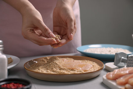 Making schnitzel. Woman coating slice of meat with bread crumbs at grey table, closeupの写真素材