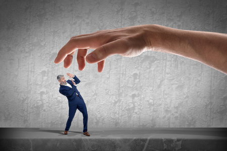 Big hand catching small scared businessman on grey background. Authority, abuse conceptsの写真素材