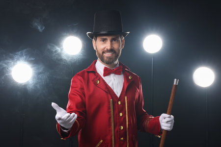 Portrait of showman in red costume, cane and hat on black background with spotlights and smoke