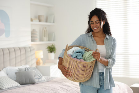 Happy woman with basket full of laundry in bedroomの写真素材