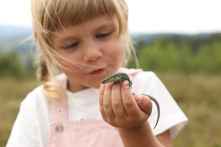 Little girl exploring lizard on blurred background. Child enjoying beautiful natureの写真素材