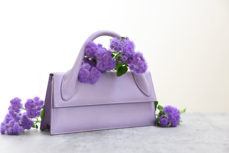 Stylish violet bag and ageratum flowers on gray table against light background, space for textの写真素材
