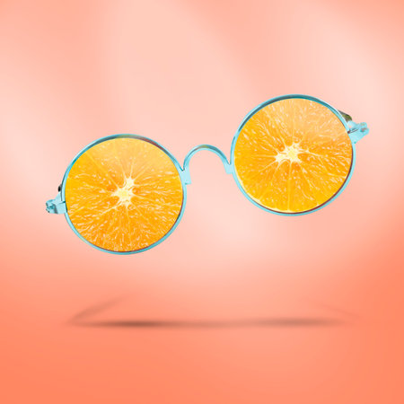 Sunglasses with juicy orange in air on coral background. Summer vibeの写真素材